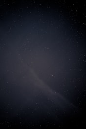 A shadowy figure writing under a glowing cosmic sky filled with stars and nebulae.