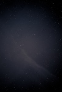 A shadowy figure writing under a glowing cosmic sky filled with stars and nebulae.