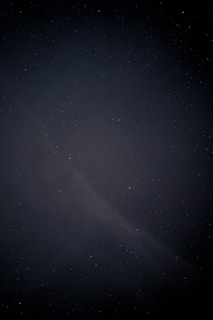 A dark night sky filled with numerous small, faint stars scattered across the expanse. A subtle, dimly lit nebula-like structure is visible, adding a sense of depth and mystique.