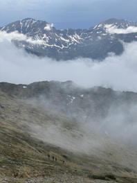 Travelers hiking through lush green mountains with misty peaks in the background.