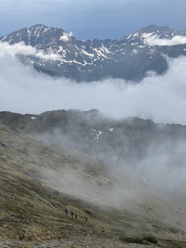 Travelers hiking through lush green mountains with misty peaks in the background.