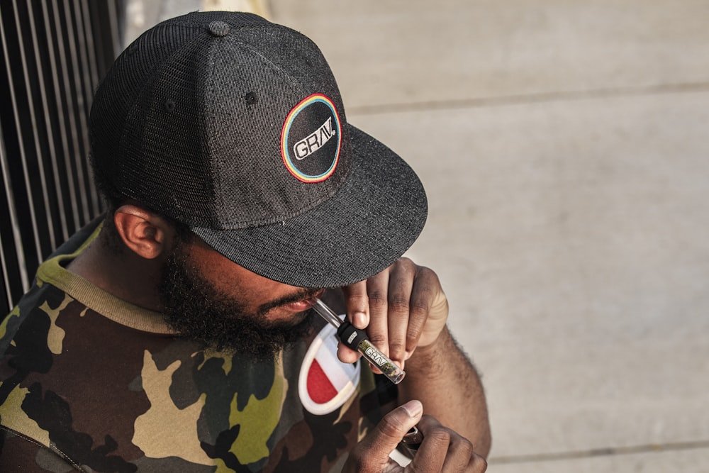 homem no chapéu de camuflagem preto e verde segurando smartphone preto e branco