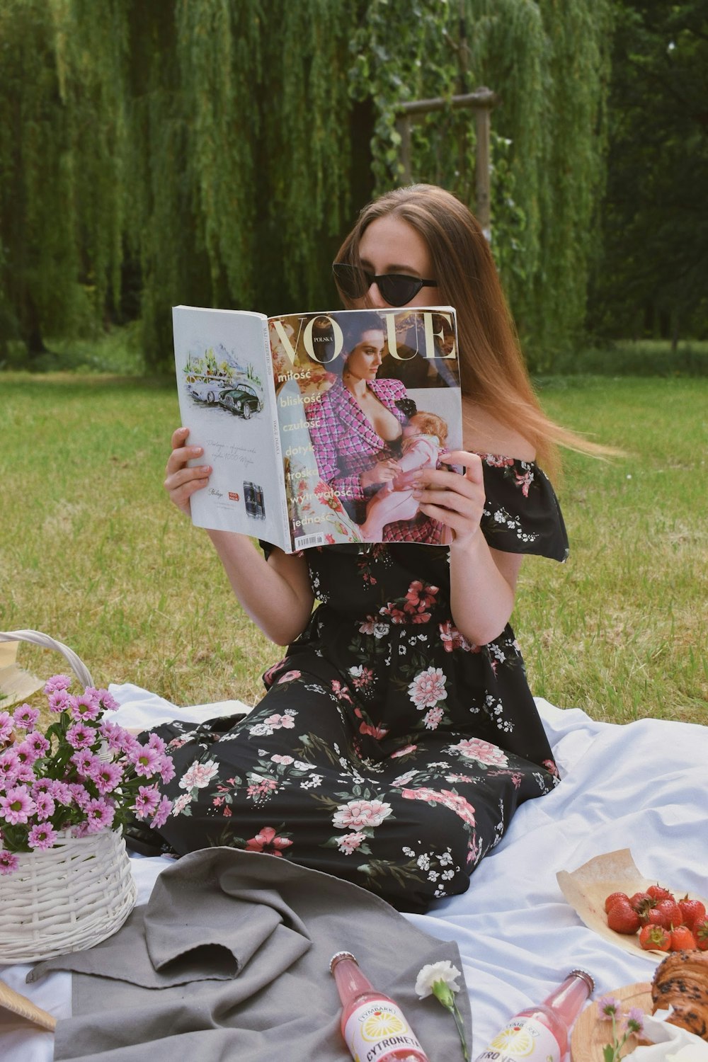 woman in black and white floral dress holding book sitting on white textile