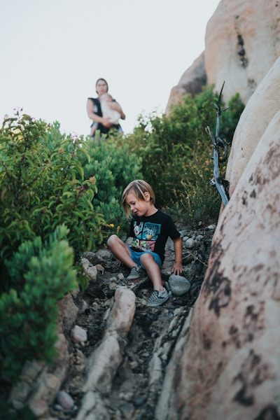 boy in blue crew neck t-shirt sitting on rock during daytime