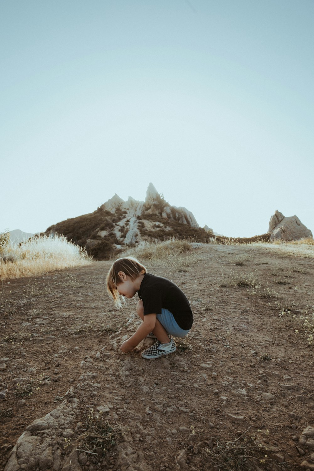 woman in black t-shirt and blue shorts sitting on ground during daytime