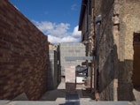 A construction site showcasing an unfinished building project with exposed brick walls and a clear blue sky in the background. The image features stacked bricks and partially constructed walls with visible pipes and construction materials.