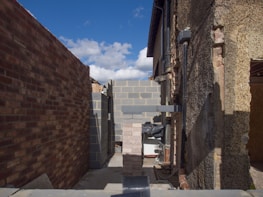 A construction site showcasing an unfinished building project with exposed brick walls and a clear blue sky in the background. The image features stacked bricks and partially constructed walls with visible pipes and construction materials.