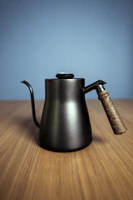 Close-up of a stylish, matte-finish kettle with smooth curves and a wooden handle on a marble countertop.