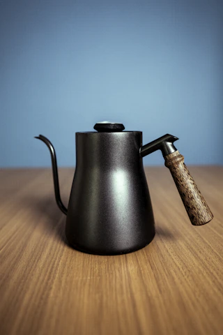 Close-up of a stylish, matte-finish kettle with smooth curves and a wooden handle on a marble countertop.