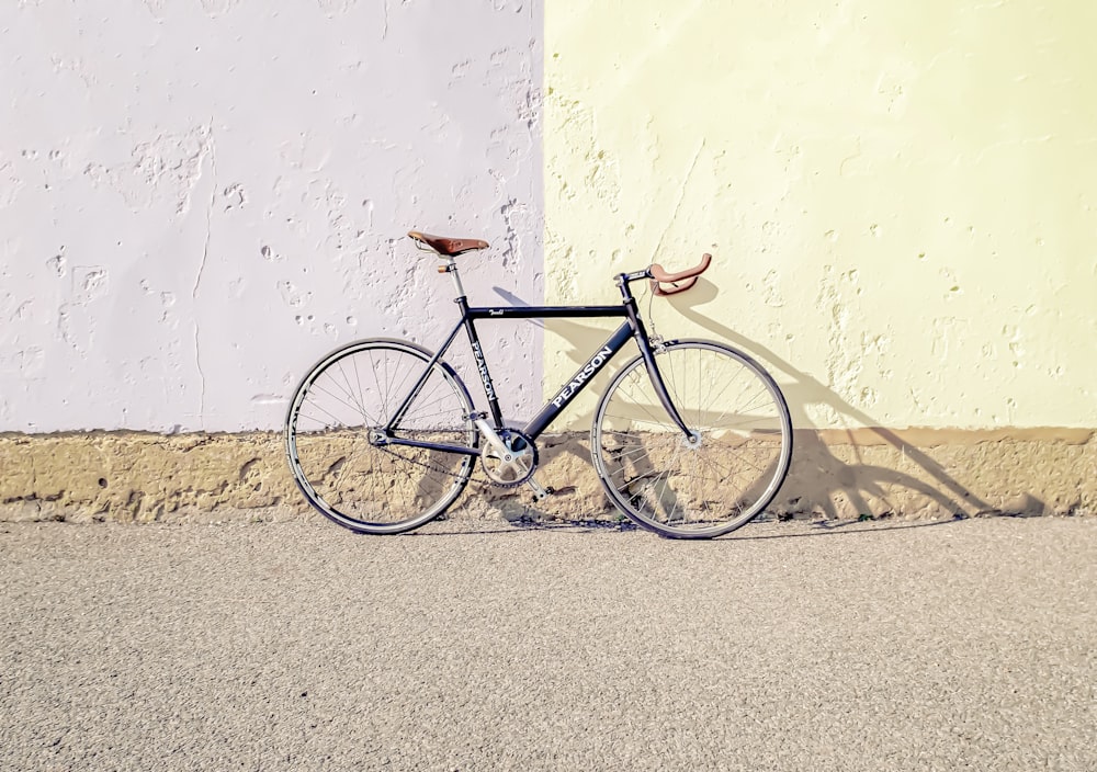 Bicicleta urbana negra y gris apoyada en una pared blanca