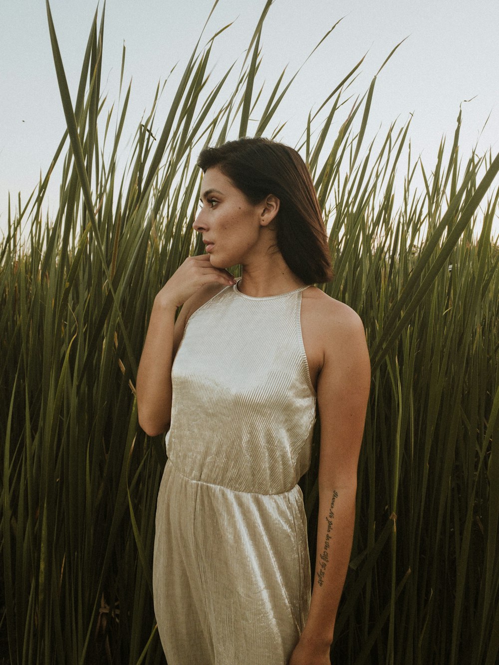 woman in white tank top standing near green grass during daytime