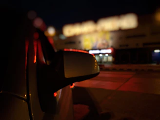 Close-up of a sleek aftermarket side mirror with a glossy black finish reflecting city lights at night.