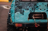 The image features the rear section of a rugged off-road vehicle with a distressed blue and black paint job. There is visible rust and wear on the metal surface, and a red tow hook is attached to a winch on the back.