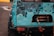 The image features the rear section of a rugged off-road vehicle with a distressed blue and black paint job. There is visible rust and wear on the metal surface, and a red tow hook is attached to a winch on the back.
