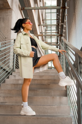 woman in white coat and black skirt sitting on brown wooden staircase