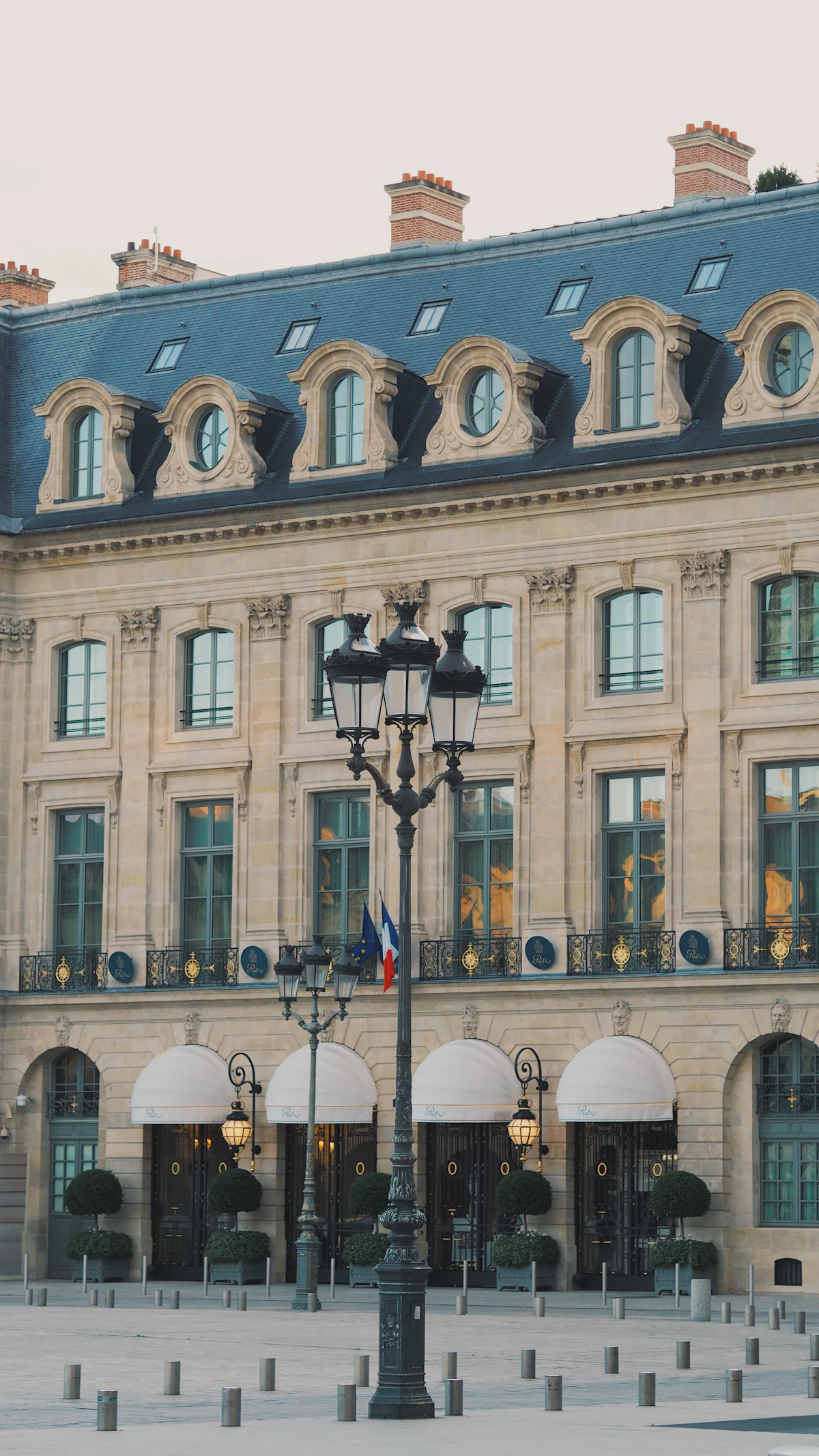 Façade d'un grand palace parisien Place Vendôme, marquises blanches et lanterne parisienne au premier plan.