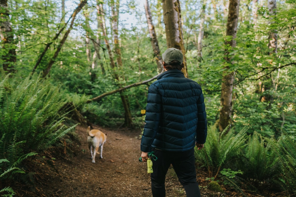 man in black bubble jacket walking with brown dog on forest during daytime