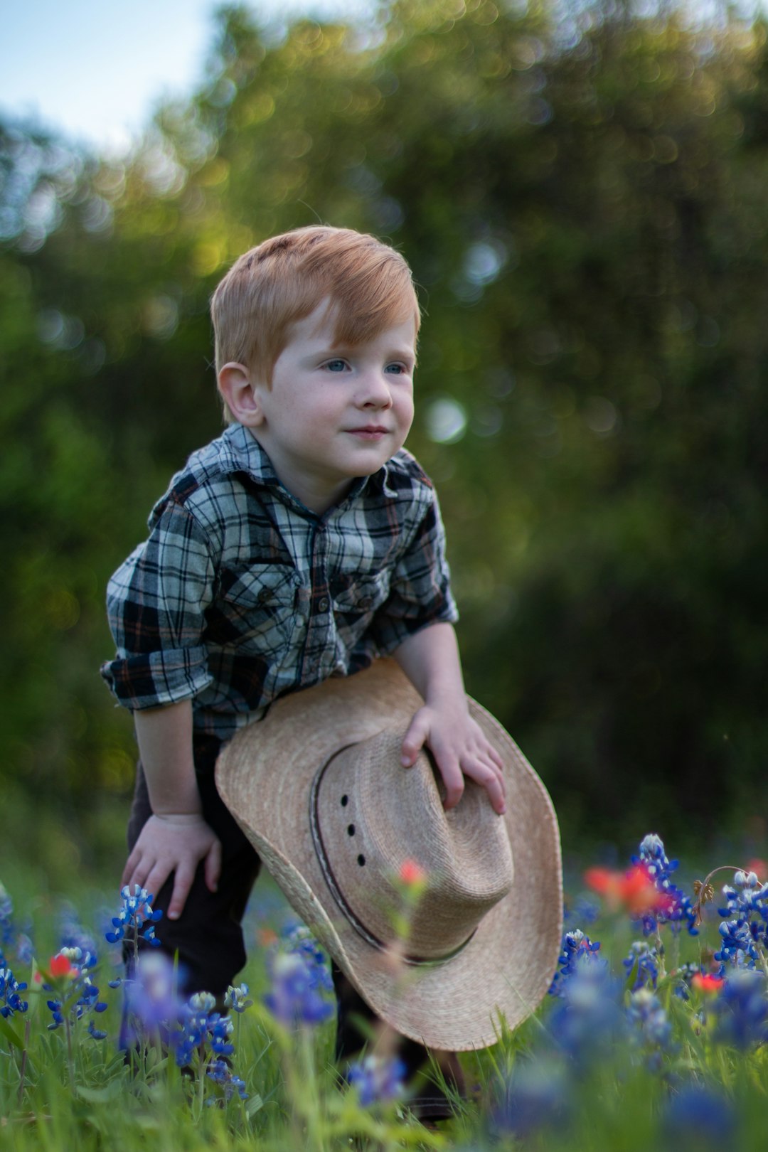 boy in blue and white plaid button up shirt and brown hat sitting on blue flowers