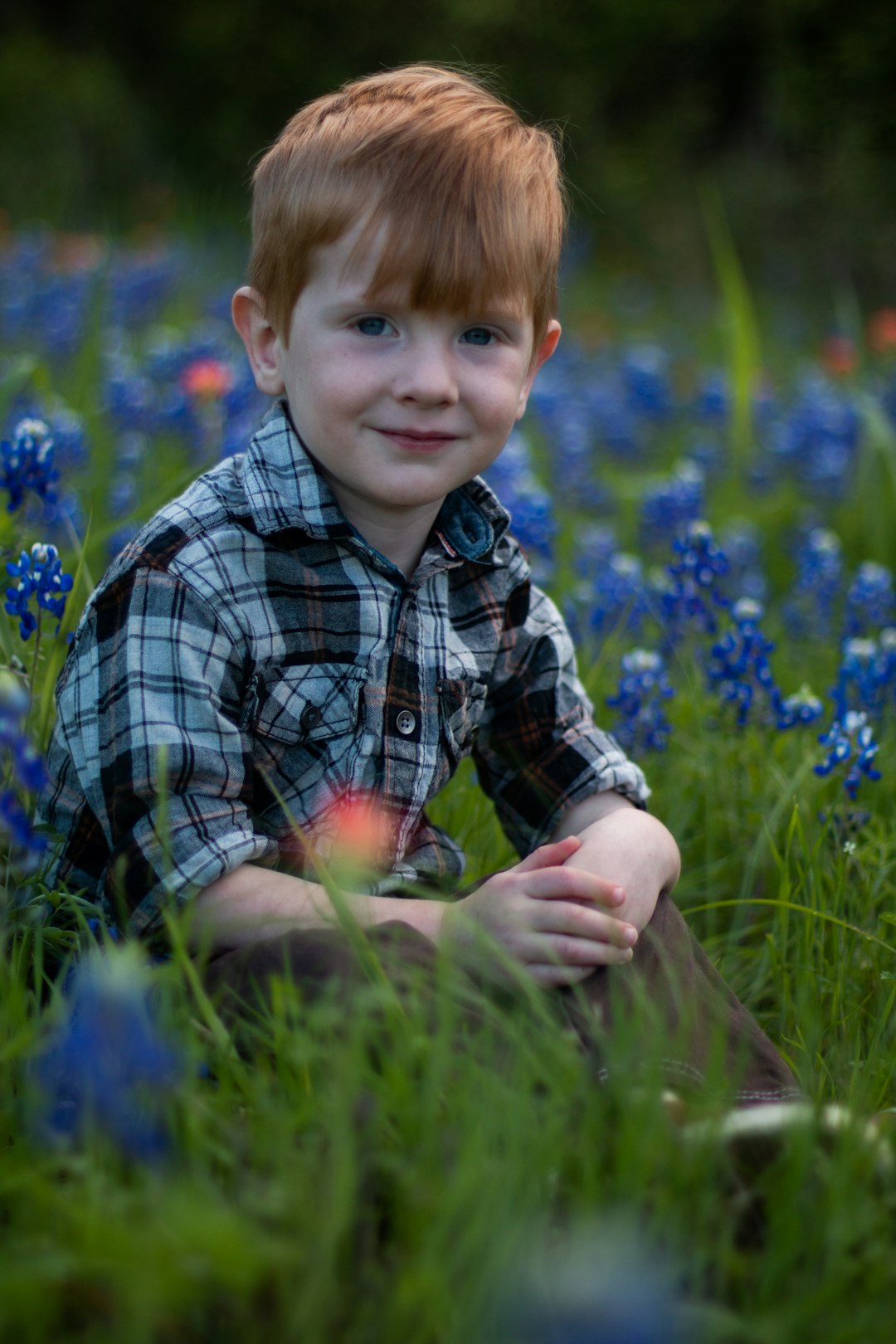 boy in blue and white plaid dress shirt sitting on green grass field during daytime