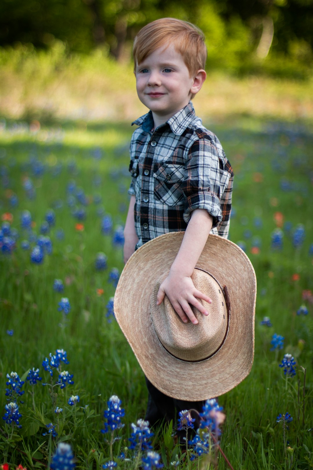 boy in blue and white plaid button up shirt and brown hat standing on green grass