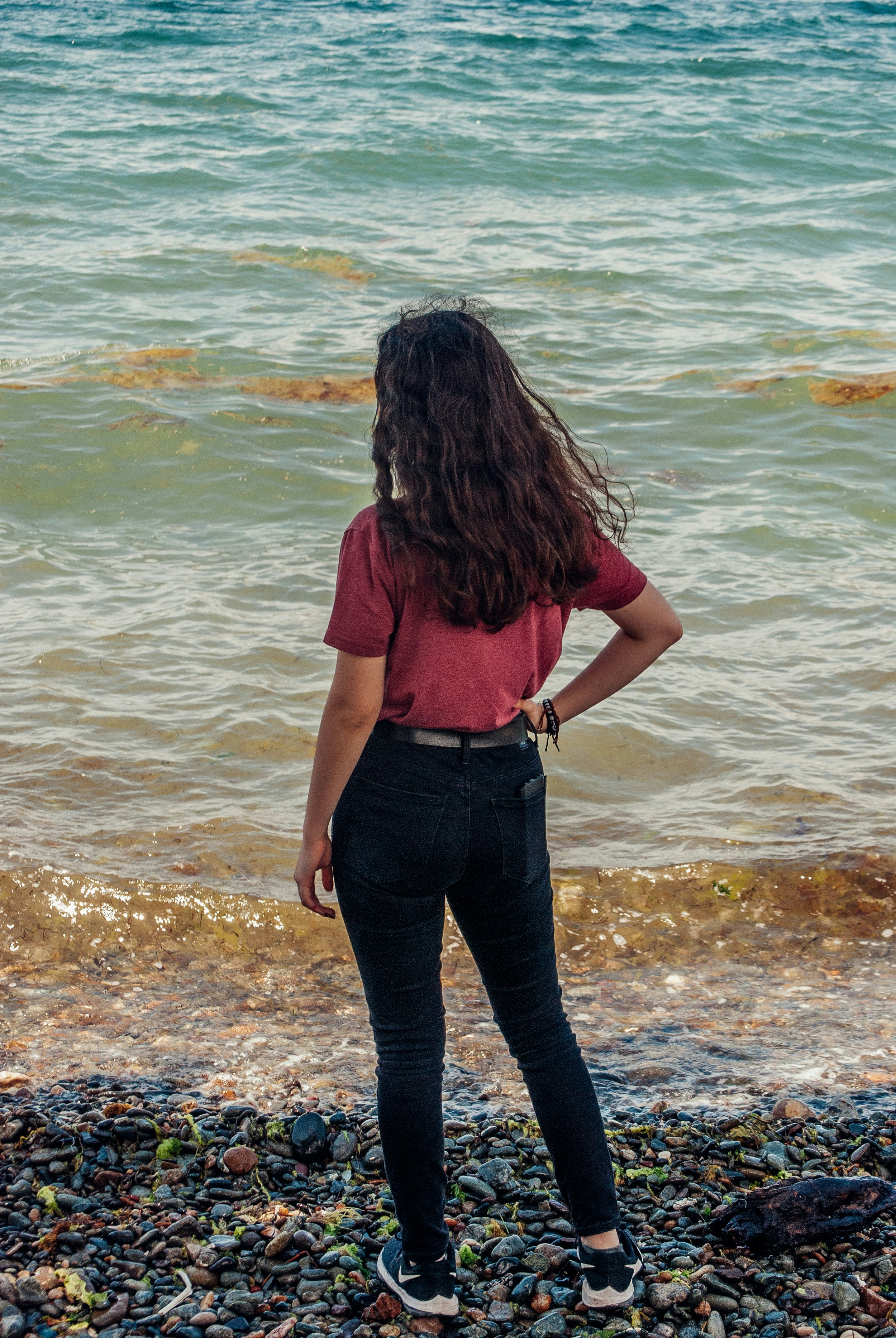 昼間に海岸に立っている赤いタンクトップと青いデニム ジーンズの女性の写真 Unsplashで見つける衣服の無料写真