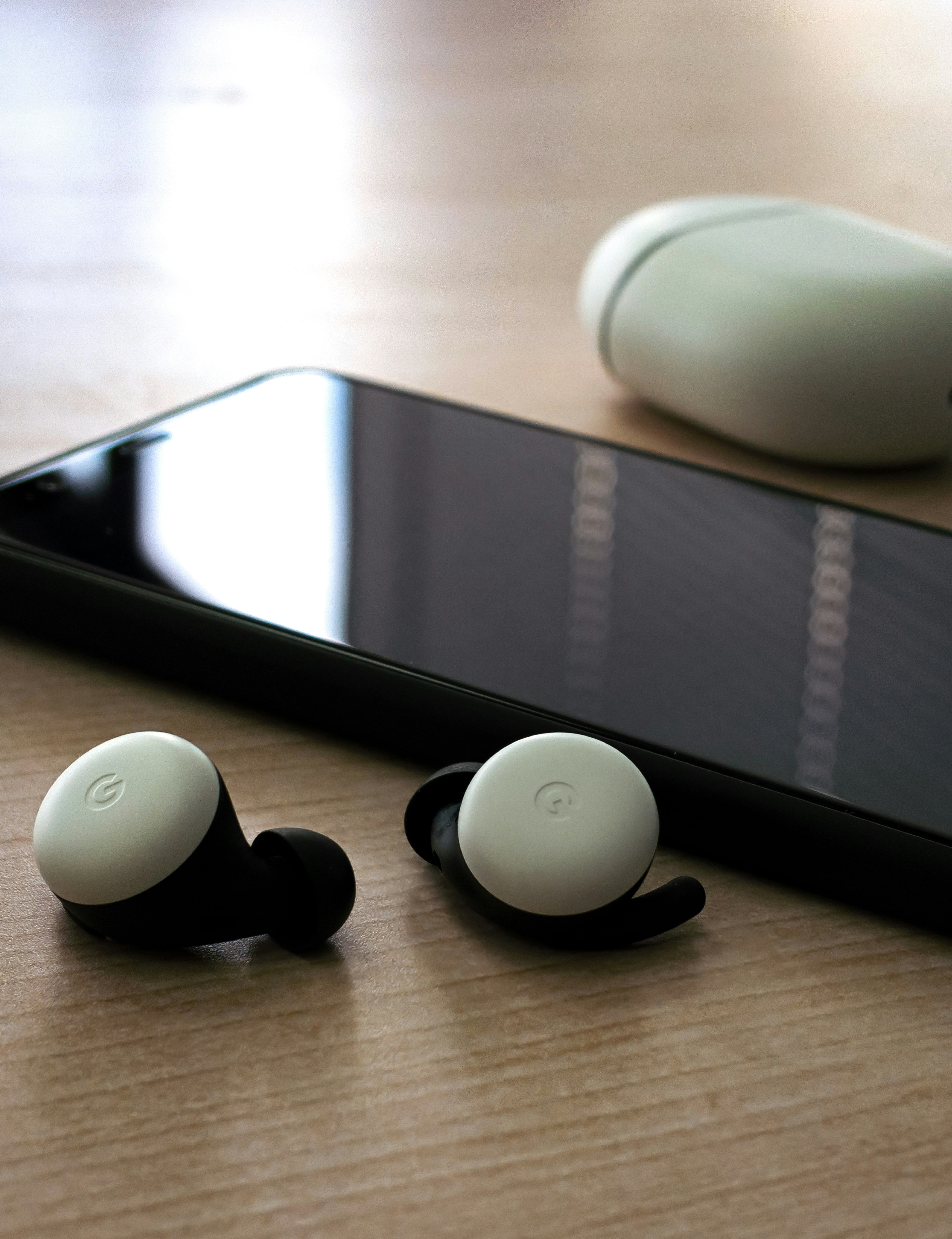 Earbuds charging case next to smartphone on wooden desk