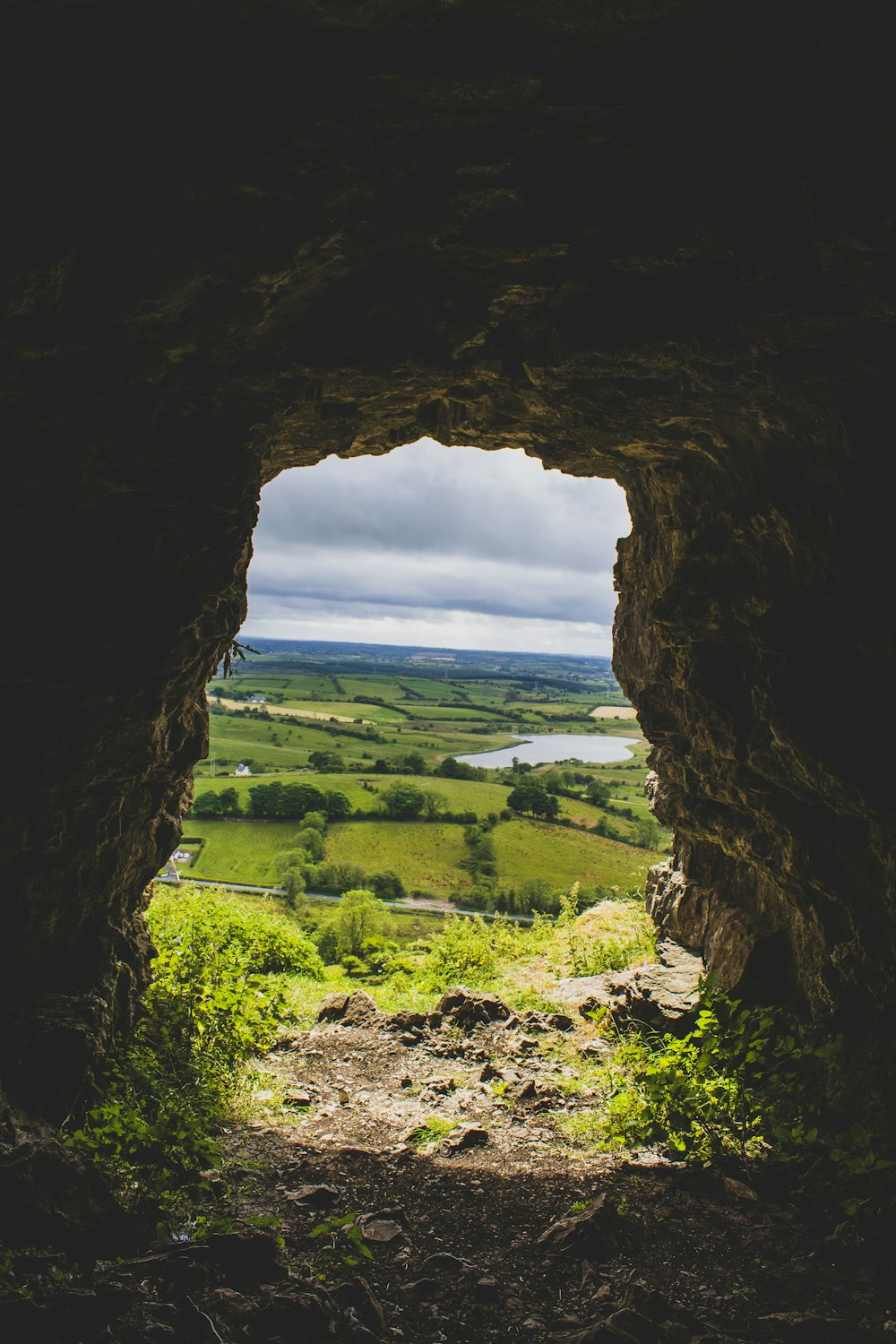 brown cave with green grass field under blue sky and white clouds during daytime