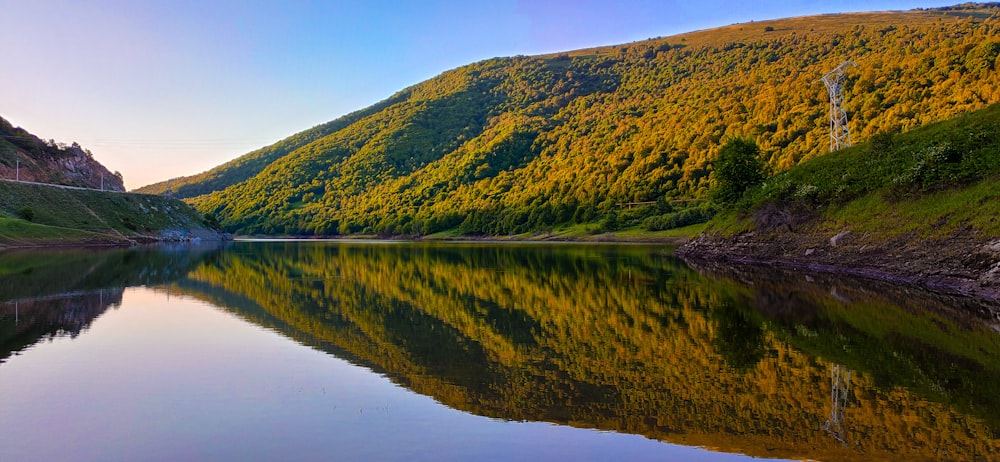 green and brown mountain beside lake under blue sky during daytime