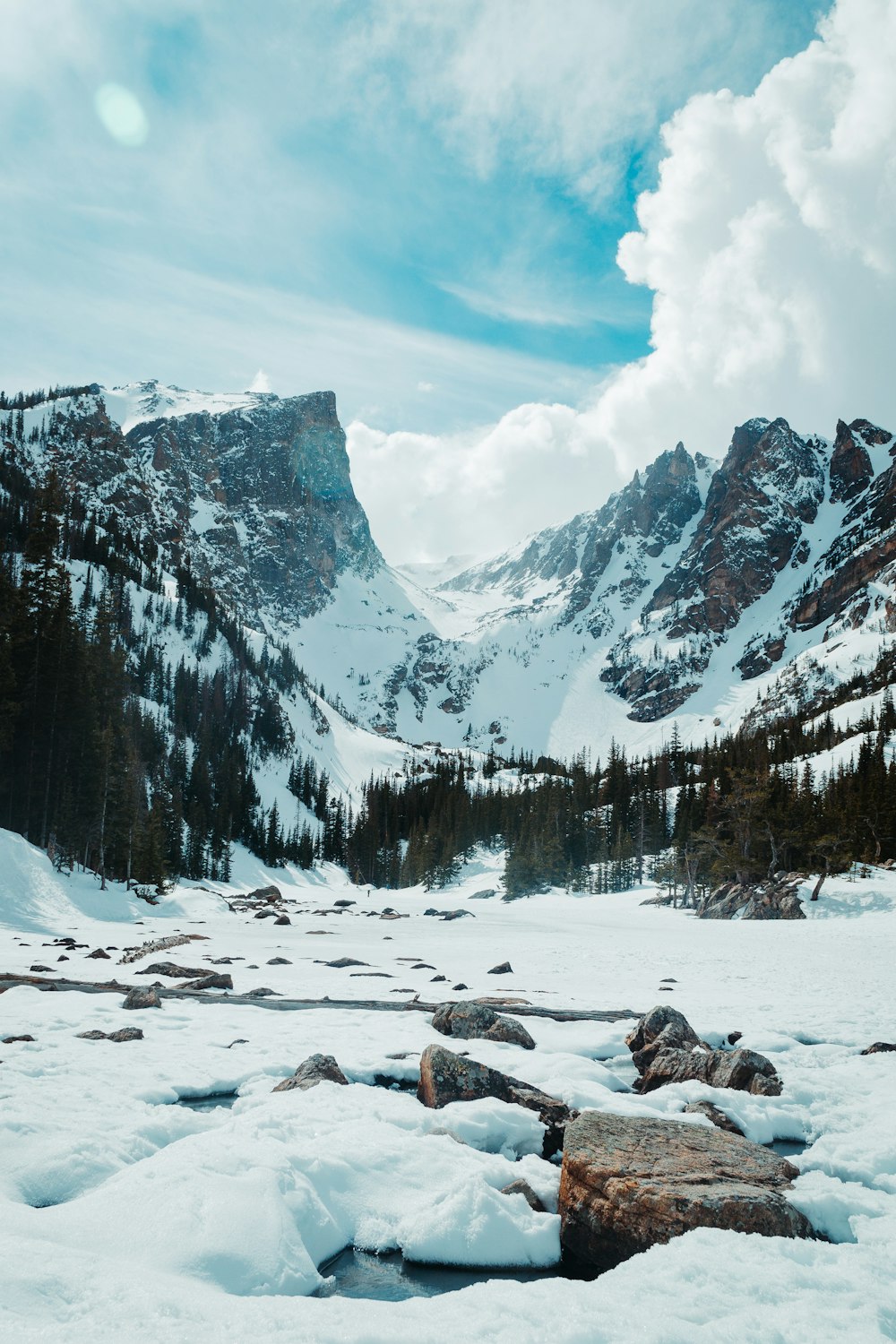 snow covered field and trees near mountain under white clouds and blue sky during daytime