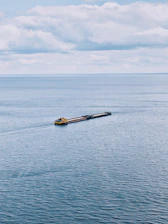 A sturdy tugboat guiding a large vessel through calm ocean waters under a clear sky.
