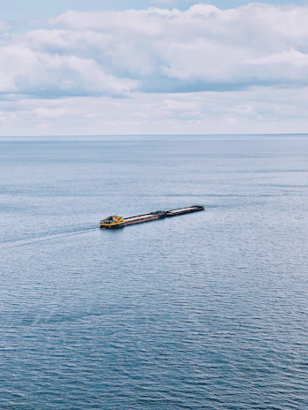 A sturdy tugboat guiding a large vessel through calm ocean waters under a clear sky.