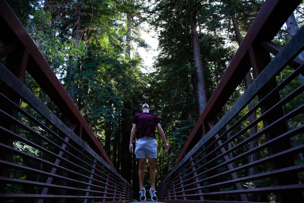 man in purple t-shirt and black shorts walking on brown wooden bridge
