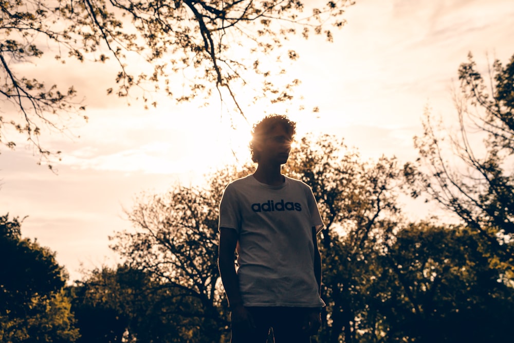man in white and black crew neck t-shirt standing near trees during daytime