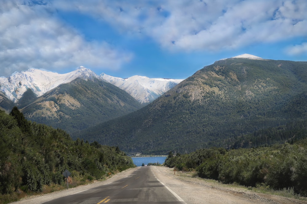 gray concrete road between green trees and mountains under blue sky and white clouds during daytime