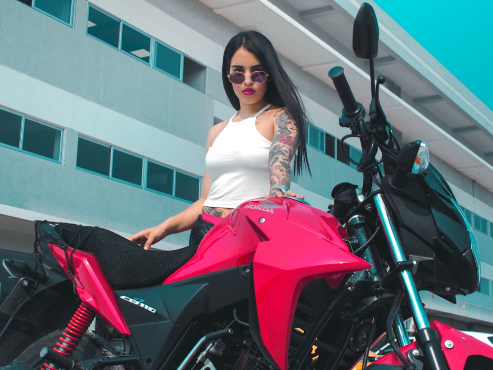 woman in white sleeveless dress standing beside red and black motorcycle during daytime