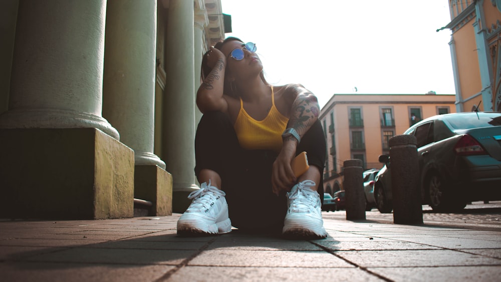 woman in yellow tank top and black tank top sitting on brown wooden bench during daytime