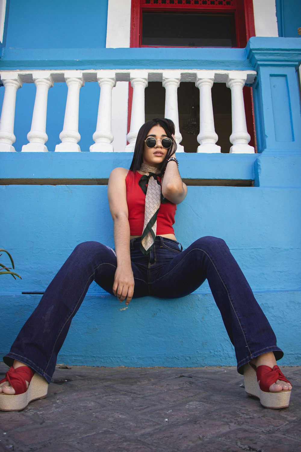 woman in orange tank top and blue denim jeans sitting on blue concrete floor