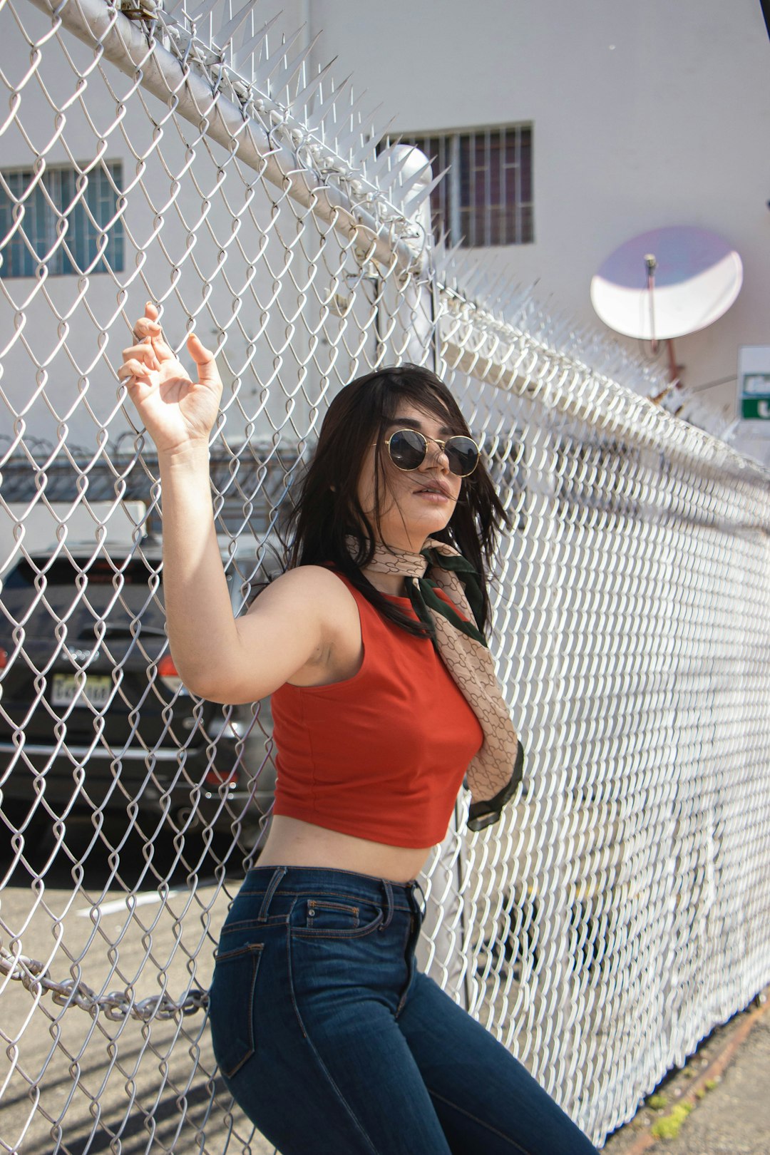 woman in red tank top and blue denim shorts leaning on gray metal fence during daytime