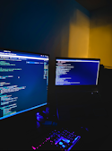 A dimly lit hacker workspace with multiple monitors displaying code.