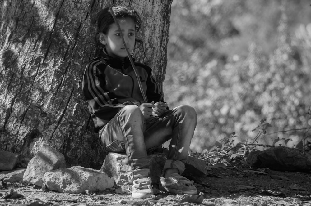 grayscale photo of boy sitting on rock