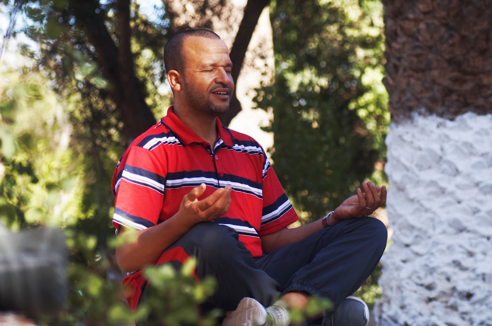 man in red and blue striped polo shirt sitting on green grass field during daytime