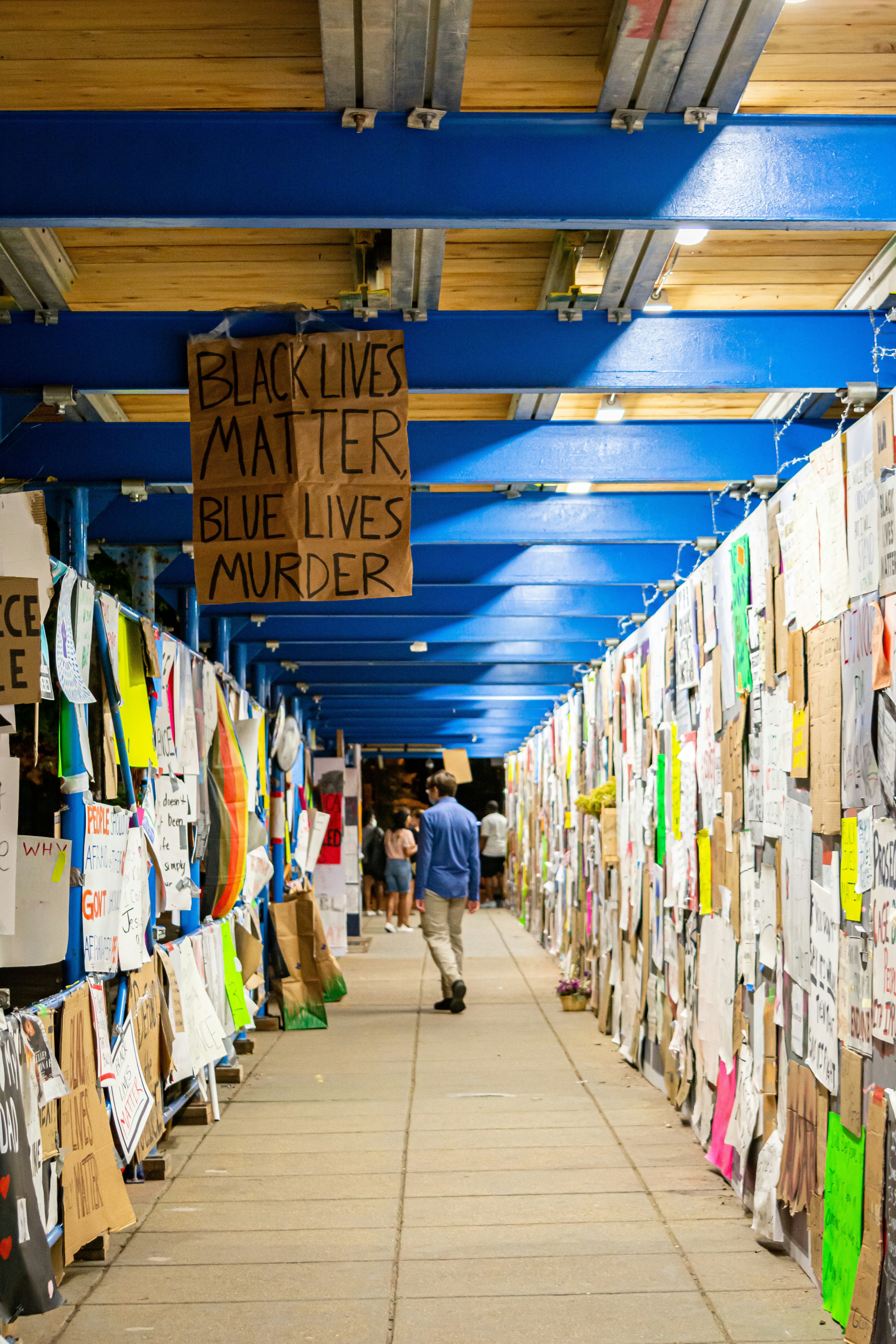 people walking on street with assorted colored clothes hanging on wall during daytime