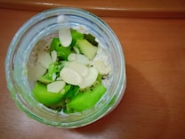 A jar of overnight oats is topped with fresh kiwi slices and almond slivers. The oats appear creamy and are placed in a clear glass jar, situated on a wooden surface.