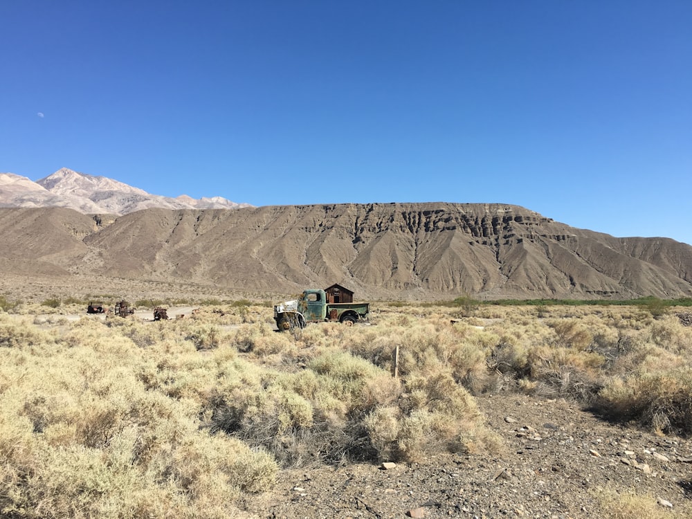 green and black truck on brown grass field near brown mountain under blue sky during daytime