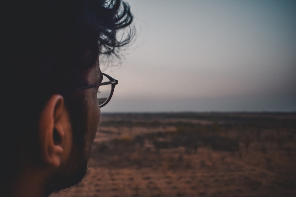 a man with glasses looking out over a desert