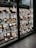 A display window with neatly arranged plastic food models representing various Japanese dishes. The models are placed on shelves, each accompanied by a label with descriptions and prices. The setup is in a traditional Japanese style, featuring wooden frames and a tiled roof.