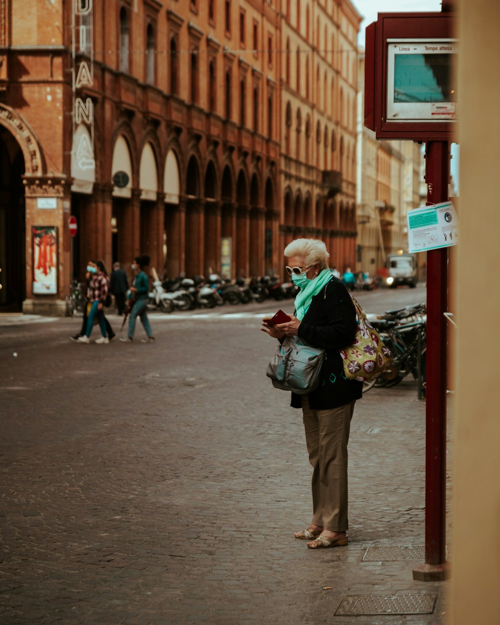 woman in green jacket and brown pants standing on sidewalk during daytime