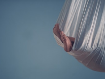 A pair of small feet peeking out from a cream-colored fabric sling against a soft blue background.