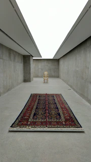 Finished hand-woven rug laid out in a minimalist space with charcoal walls and soft gold accents.