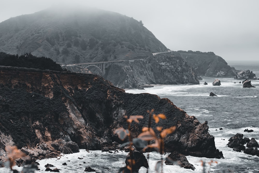 person in black jacket sitting on rock near body of water during daytime